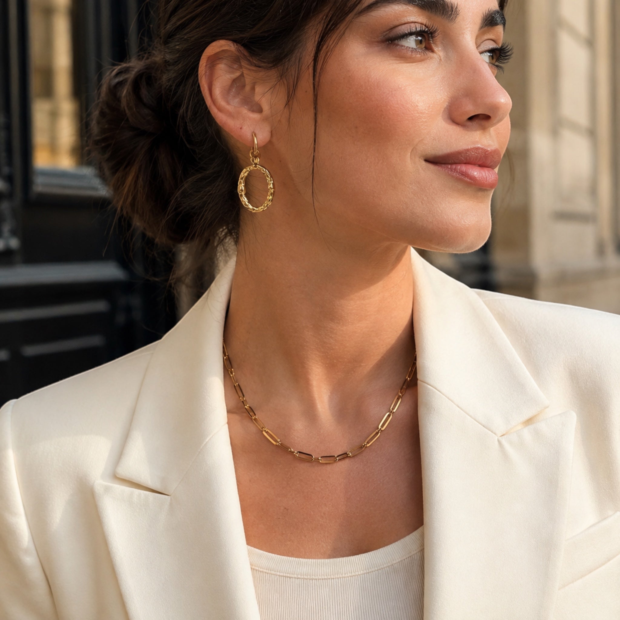 Ma boutique Halo gold textured oval interchangeable earring charm worn by a woman in a white blazer