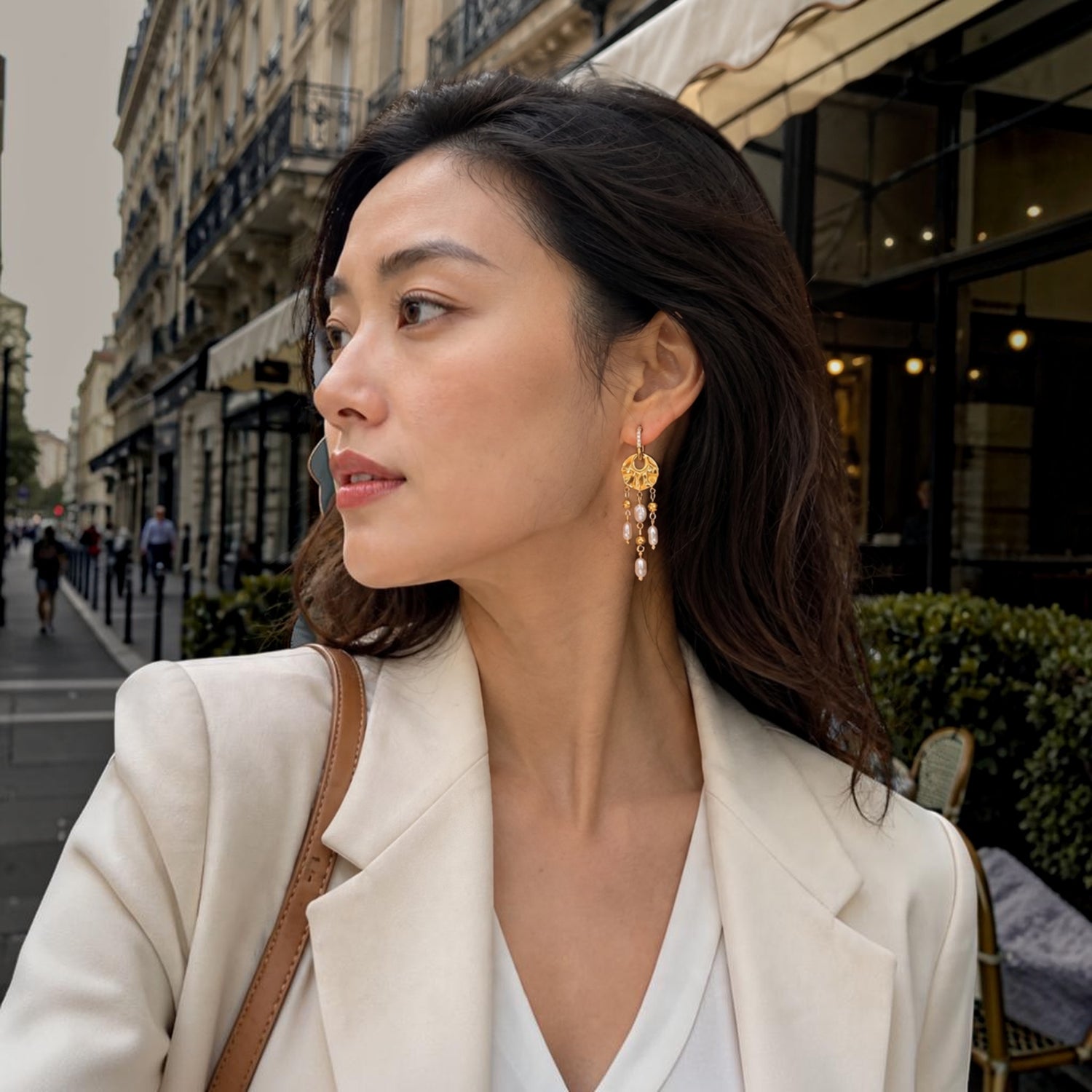 Ma boutique Néréide gold earring charm with pearl tassels worn by a woman in a white blazer on a city street